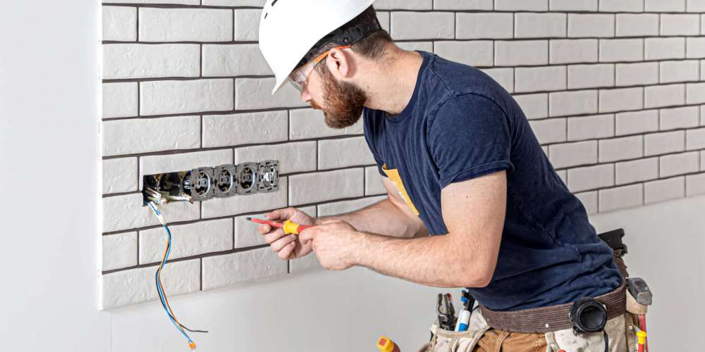 Electrician construction worker with a beard in overalls during the installation of sockets. Home renovation concept.